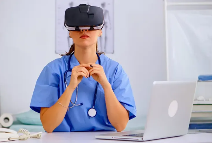 Nurse wearing a VR headset and sitting down at desk with a laptop in front of her