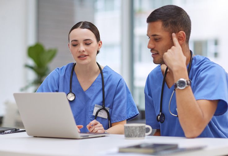 Two nursing students talking and sitting down looking at a laptop